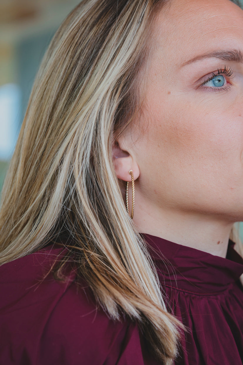 Boucles d’oreilles créoles torsadées dorées, anneau fin avec texture, portées sur le lobe.