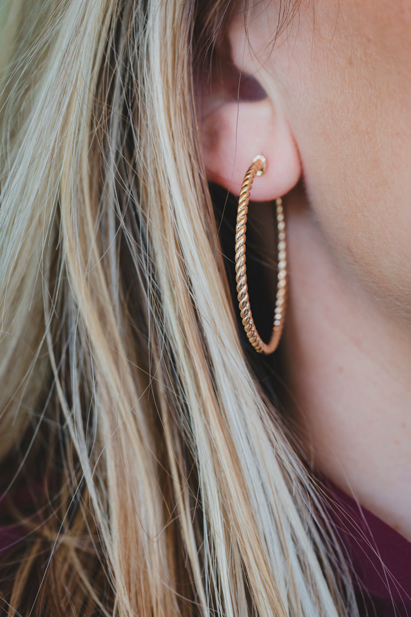Boucles d’oreilles créoles dorées torsadées, détail de l’anneau texturé sur le lobe.