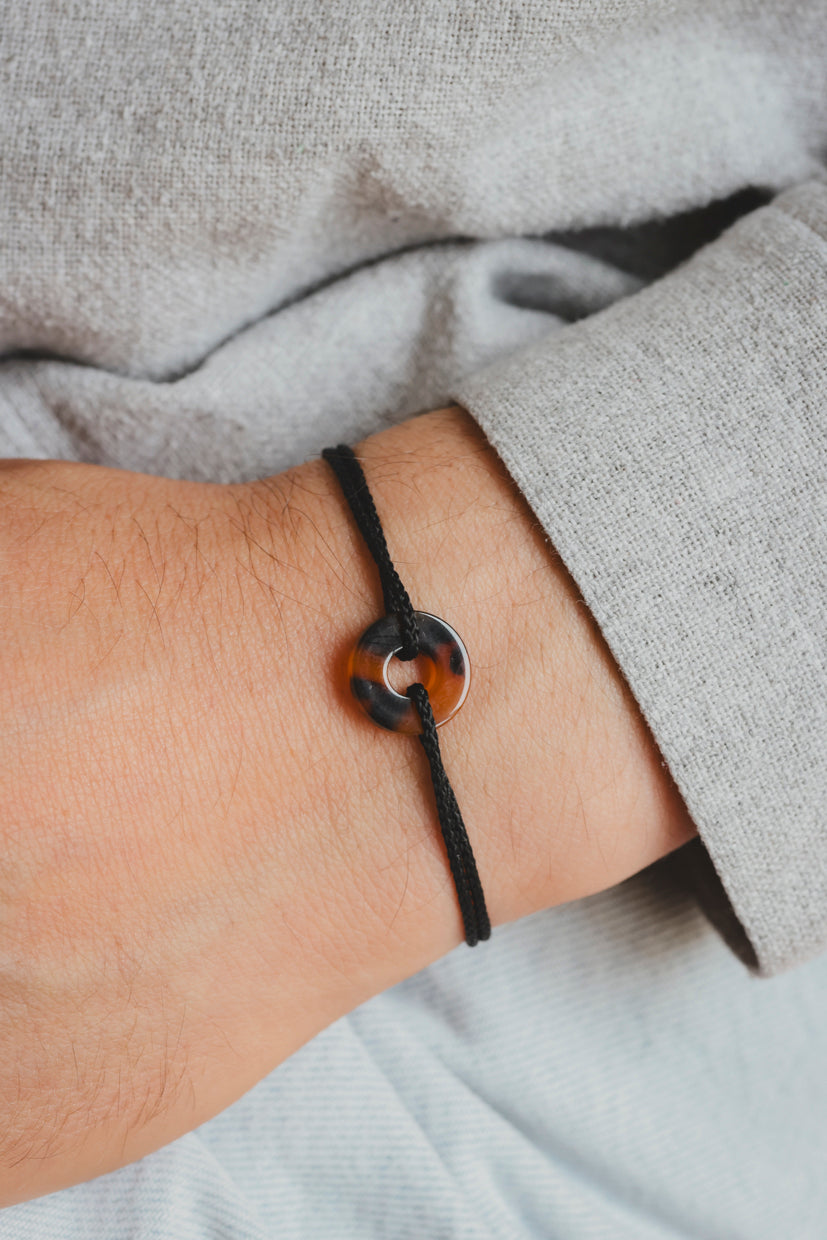 Bracelet en paracorde noir avec pendentif écaille ronde orange sur le poignet