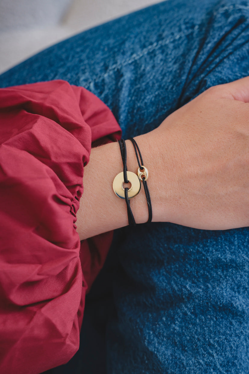 Bracelet à corde noire avec cercle doré et pendentif cible, porté au poignet