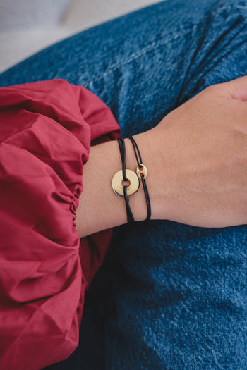 Bracelet à corde noire avec cercle doré et pendentif cible, porté au poignet