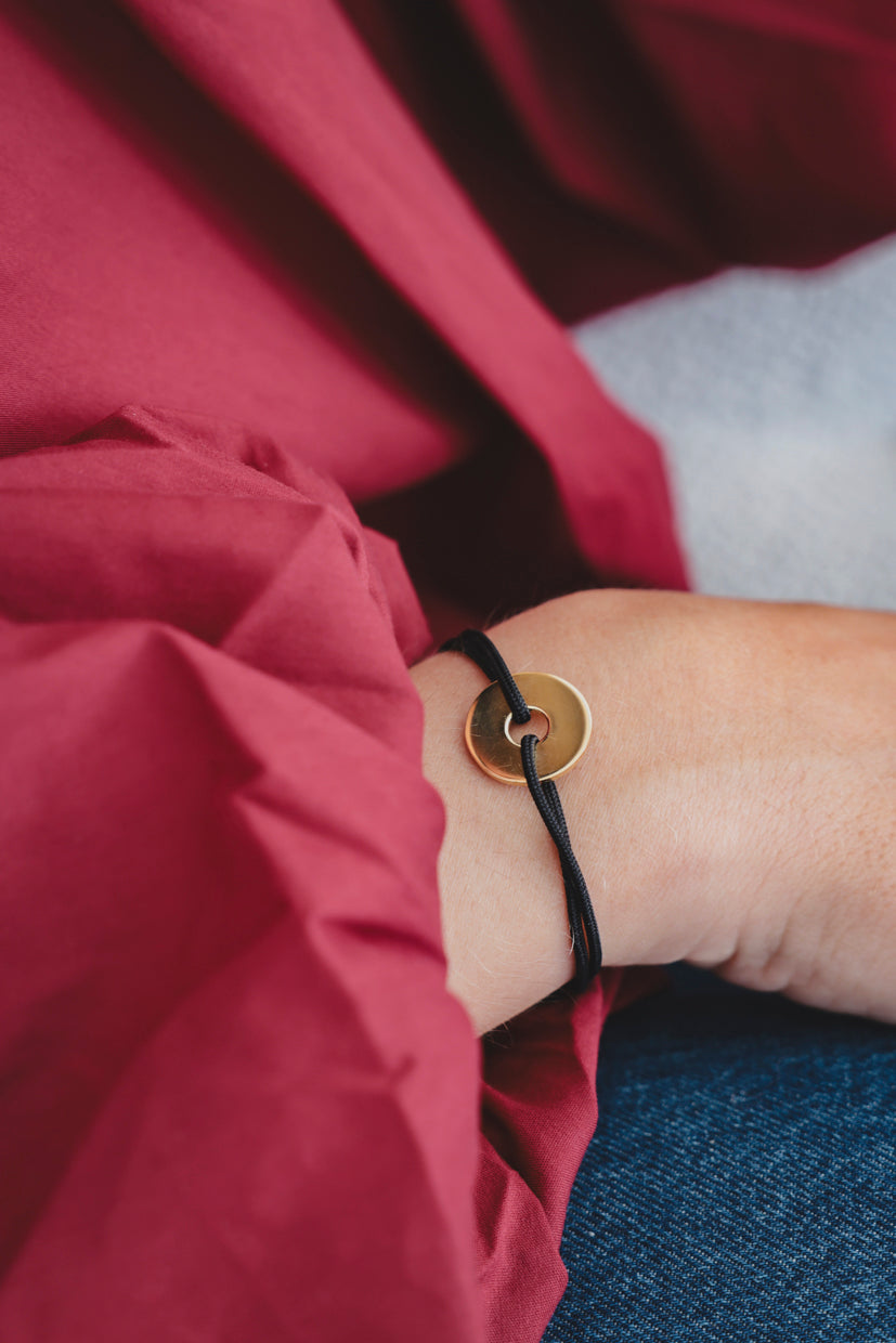 Bracelet corde noire avec anneau doré et pendentif cible, porté au poignet