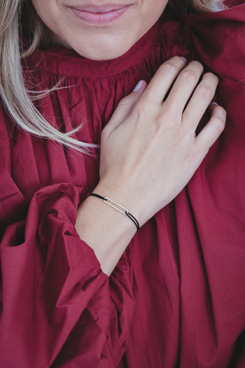 Bracelet à cordon noir avec barreau métallique fin, porté près de l’avant-bras