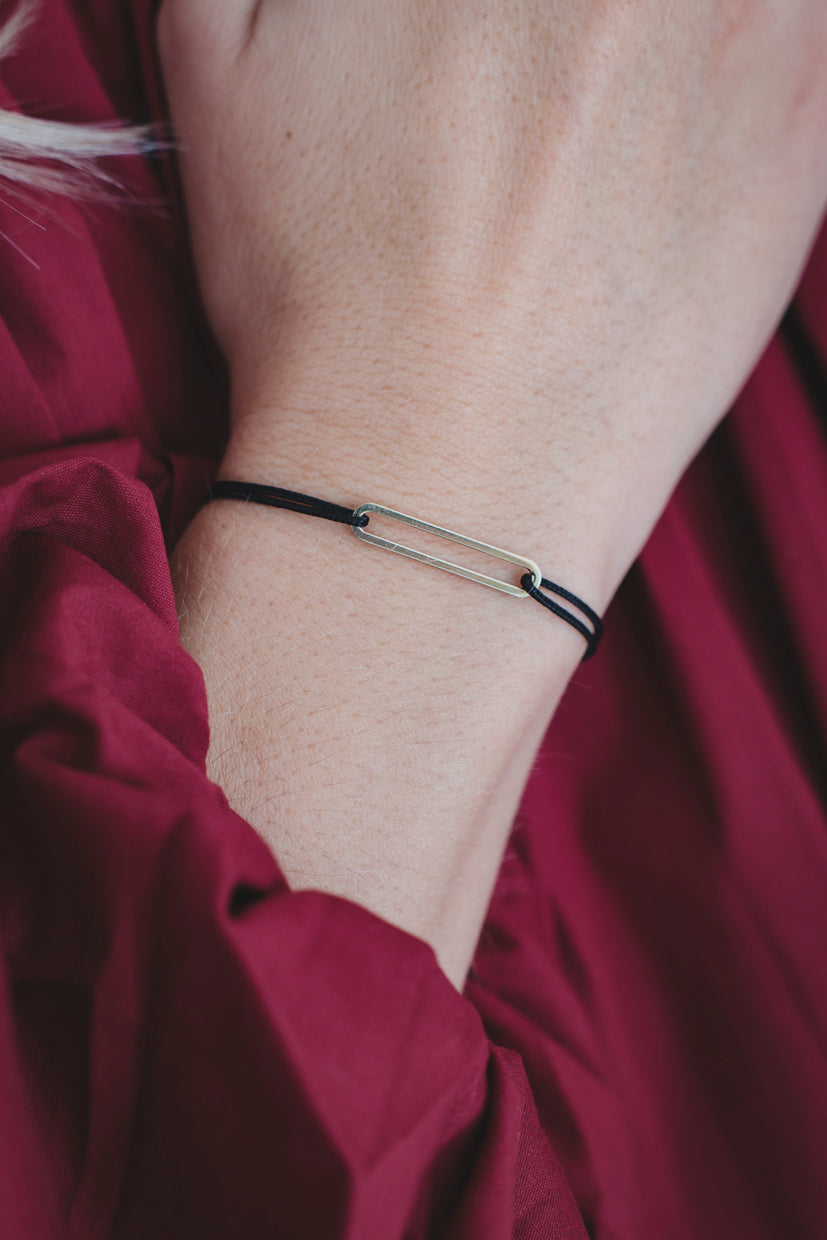 Bracelet fin à cordon noir et deux petites perles métalliques, porté au poignet