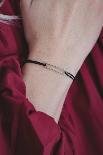 Bracelet fin à cordon noir et deux petites perles métalliques, porté au poignet