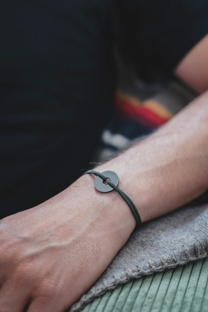 Bracelet La Cible argent 925 rhodié, pastille ronde et cordon sombre au poignet.