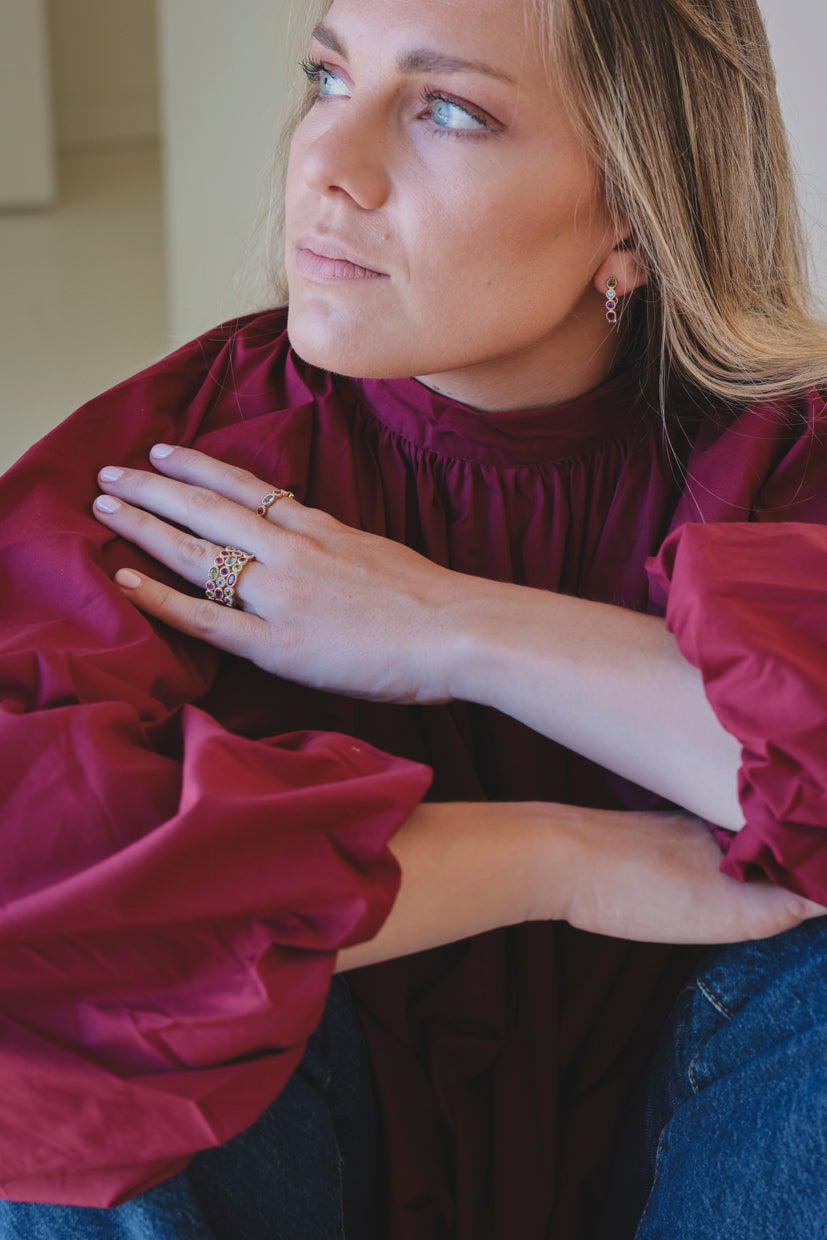 Bague ajourée dorée sertie de pierres multicolores, portée sur le doigt