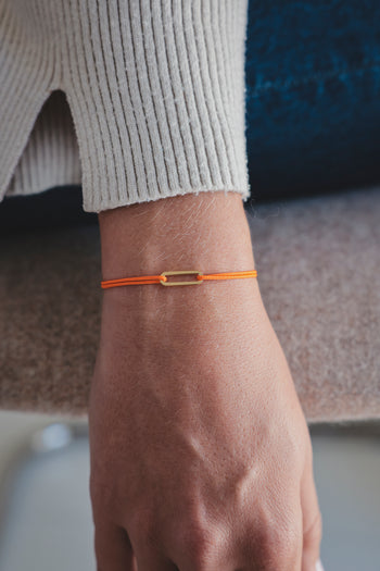Bracelet Le Petit Maillon à plaque or sur poignet, paracorde orange, gros plan