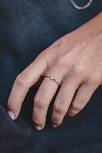 Bague dorée fine ornée d’une pierre centrale, portée sur la main