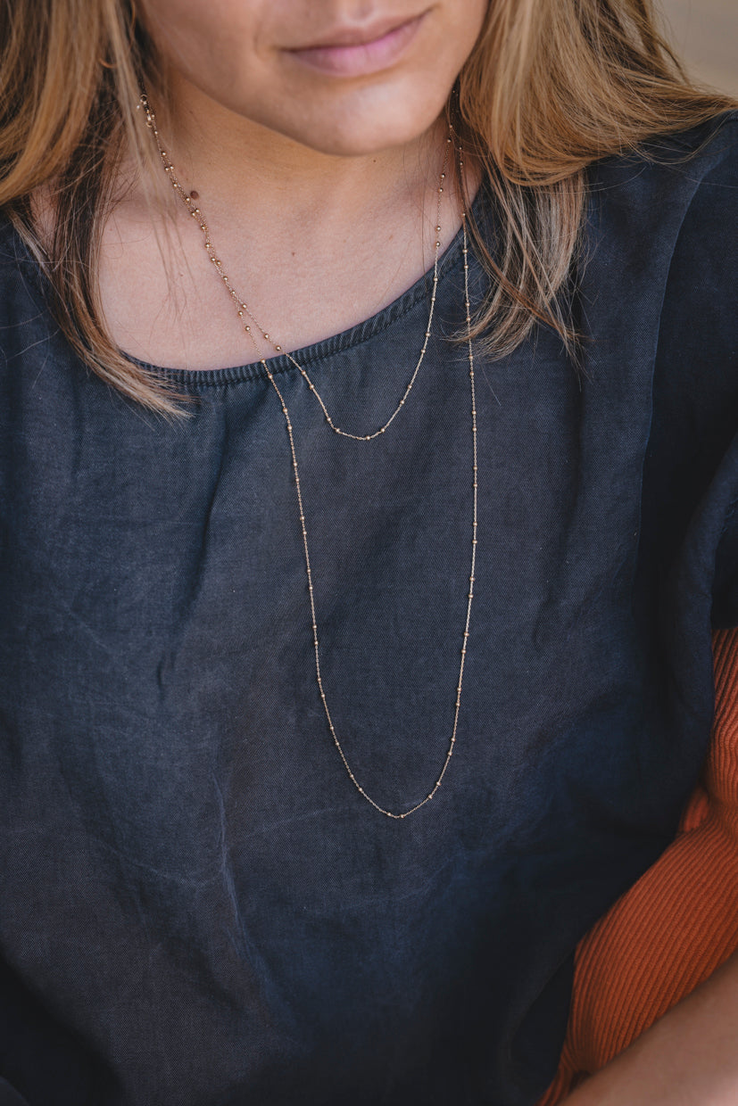 Collier sautoir à double rang fin en métal doré, porté près du cou