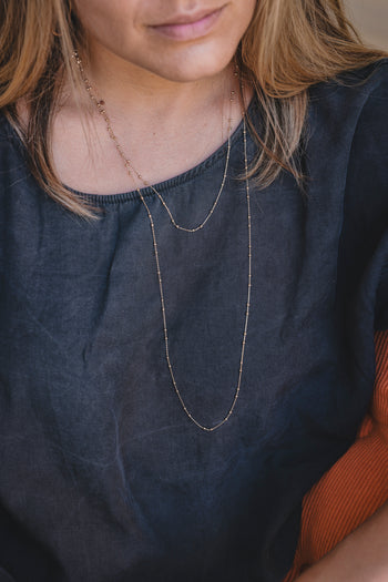 Collier sautoir à double rang fin en métal doré, porté près du cou