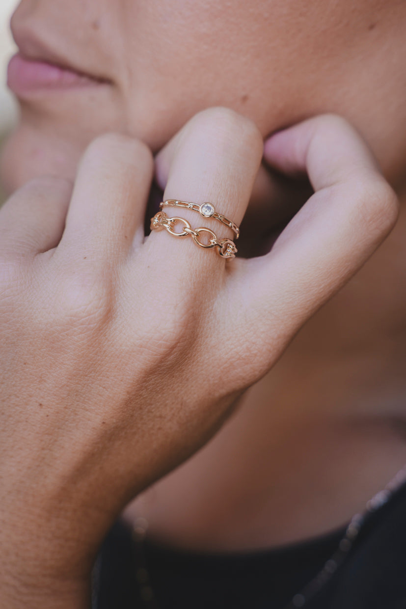 Bague dorée avec éléments chaînés et petite pierre, portée sur l’annulaire