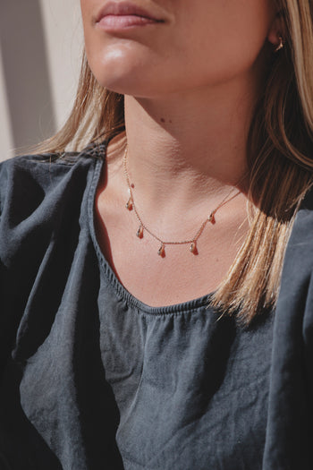 Collier Sonora porté : chaîne dorée avec pendentifs et pierres rouges, tour de cou