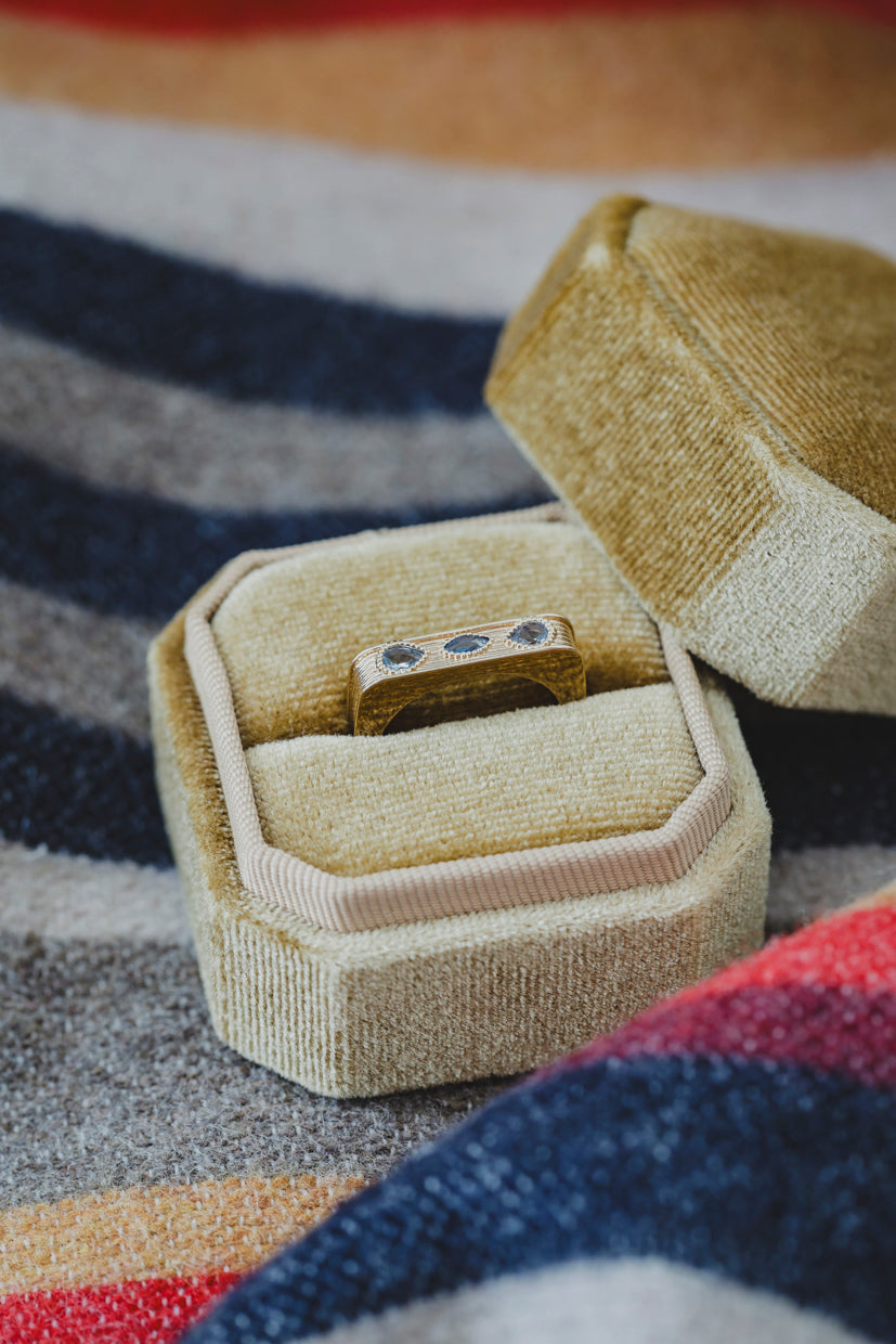 Bague Sierra dorée avec pierres bleues, dans un écrin en tissu beige.