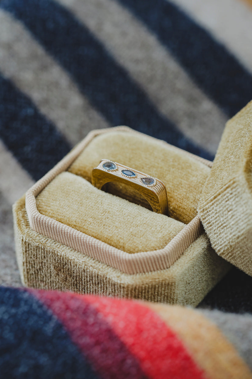 Bague Sierra dorée, pierres bleues ovales visibles, dans un écrin beige.