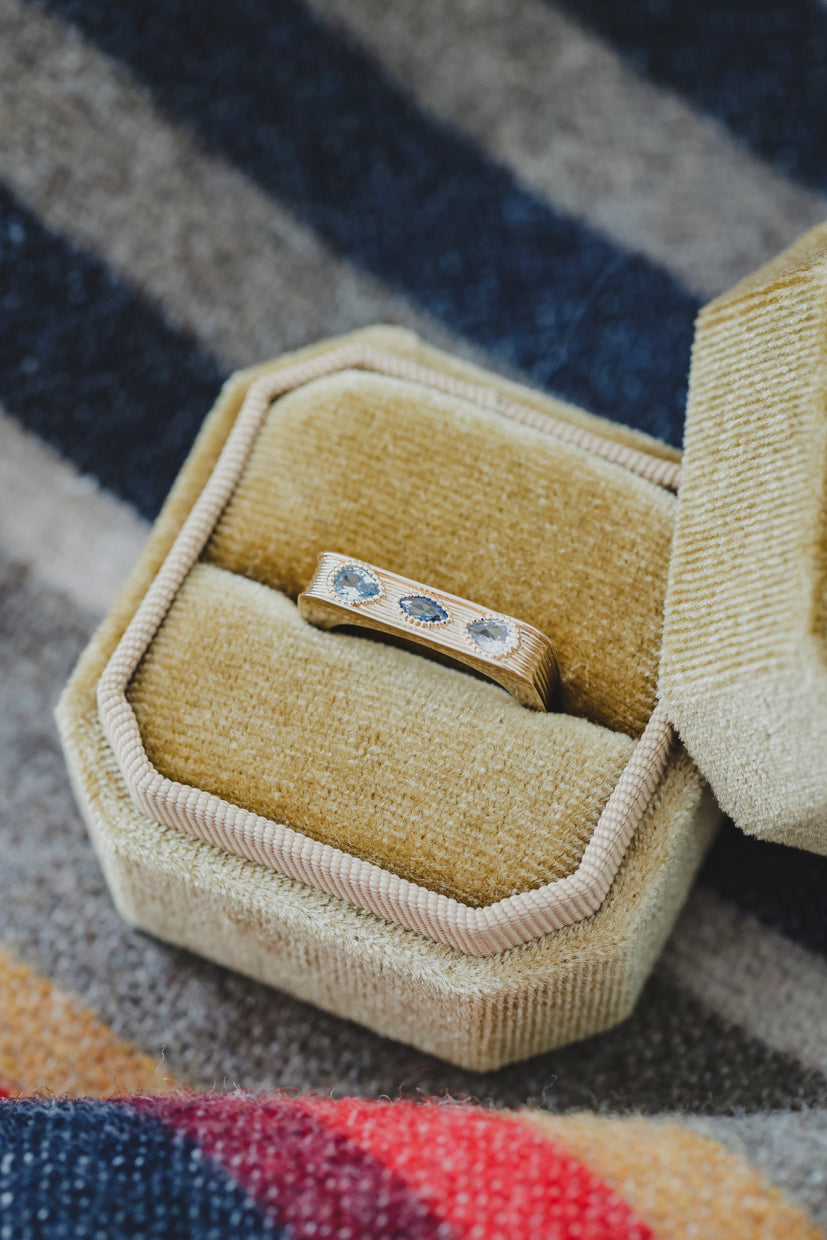 Bague Sierra en métal doré avec motif bleu, posée dans un écrin textile beige.