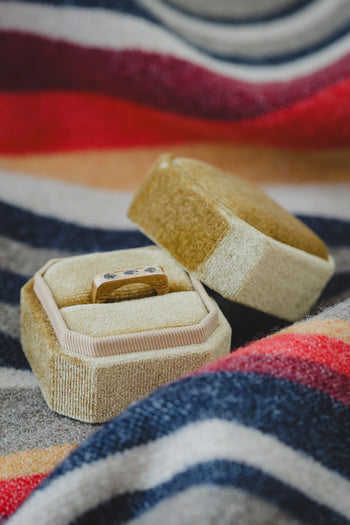 Bague Sierra dorée dans un écrin beige, deux pierres bleues visibles.