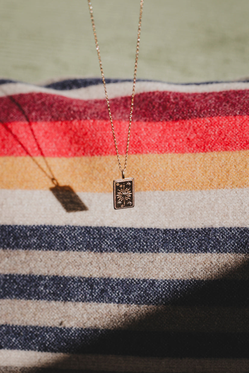 Collier Solia : pendentif rectangulaire à fond sombre et motif étoile doré sur chaîne fine.