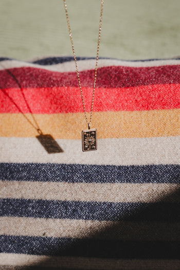Collier Solia : pendentif rectangulaire à fond sombre et motif étoile doré sur chaîne fine.